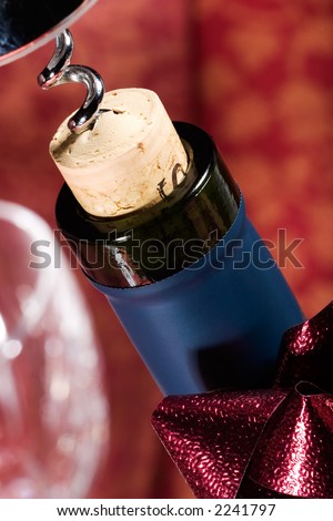 Closeup of red wine bottle neck with cork almost out and holiday ribbon