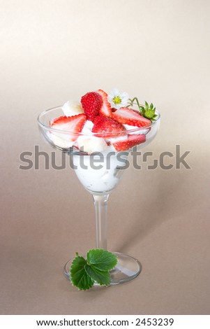 Martini glass full of pieces of fresh banana, strawberries and cream with organic yogurt decorated with strawberries flower