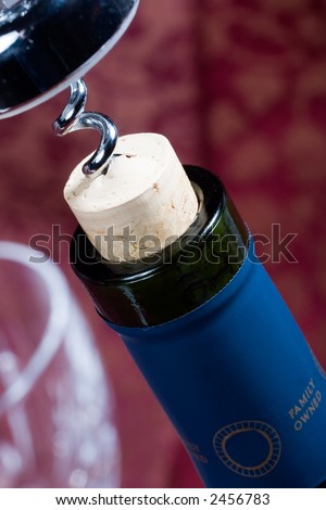 Closeup of red wine bottle neck with cork almost out and glass out of focus