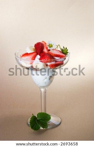 Martini glass full of pieces of fresh banana, strawberries and cream with organic yogurt decorated with strawberries flower