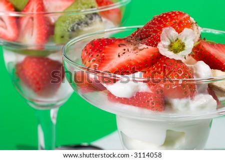Closeup of martini glass full of fresh kiwi, strawberries, bananas and cream with organic yogurt sprinkled by chocolate crumbles over green background