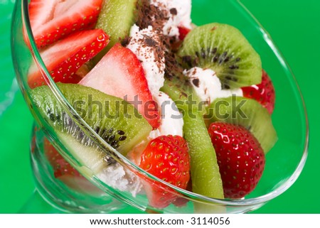 Closeup of martini glass full of fresh kiwi, strawberries and cream with organic yogurt sprinkled by chocolate crumbles over green paper background