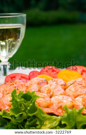 Grilled shrimps on bamboo sticks served with tomato and green saled and glass of white wine are served outside