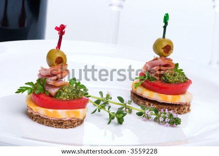 Closeup of two delicious Pesto cheese and ham canapes-sandwiches made from Pesto, cheese, ham, tomato and olive served with red wine in background