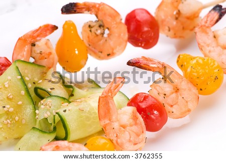 Closeup of grilled shrimps and pear tomatoes on bamboo sticks served with cucumber sesame sald in dinner setting. Shallow DOF, focus on first row.