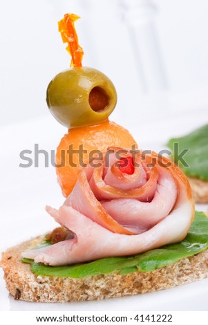 Closeup of delicious ham and melon canapes-sandwiches made from ham, melon green salad and olive over white background