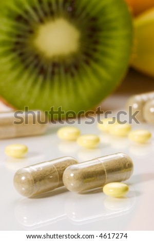 Closeup of medical pills in focus and fruits in background out of focus. Shallow DOF. Image suited for health topics about choice between medicine and healthy food