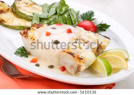 Grilled halibut with capers and pepper sauce served with lemon, lime, tomatoes and green peas
