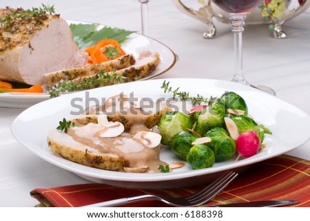 Delicious sliced garlic thyme roast pork loin with mushrooms sauce, brussels sprouts, almonds and radish ready for dinner in middle of fall arrangment table and two glasses of red wine.