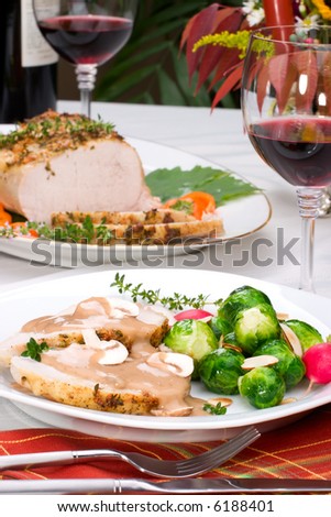 Delicious sliced garlic thyme roast pork loin with mushrooms sauce, brussels sprouts, almonds and radish ready for dinner in middle of fall arrangment table and two glasses of red wine.
