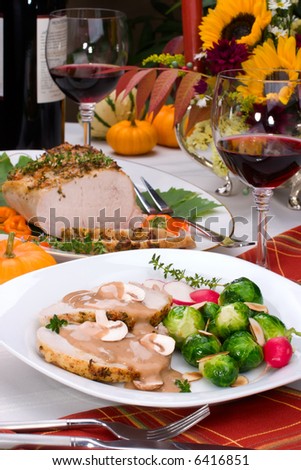 Delicious sliced garlic thyme roast pork loin with mushrooms sauce, brussels sprouts, almonds and radish ready for dinner in middle of fall arrangement table and two glasses of red wine.