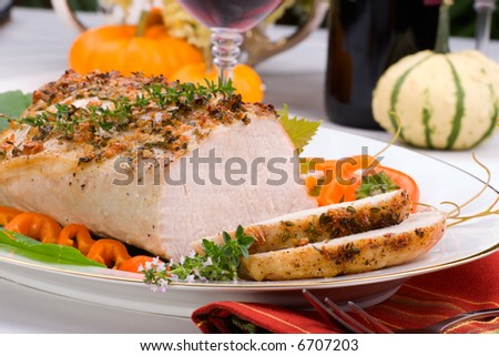 Delicious sliced garlic thyme roast pork loin is ready for dinner in middle of fall arrangement table and two glasses of red wine.