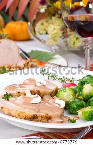 Delicious sliced garlic thyme roast pork loin with mushrooms sauce, brussels sprouts, almonds and radish ready for dinner in middle of fall arrangement table and two glasses of red wine.