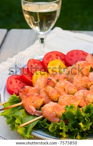 Grilled shrimps on bamboo sticks served with limes, thyme twig and glass of white wine are served outside