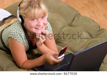 Blond cute teenager girl on sofa with laptop and a cell phone