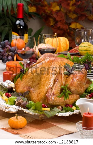 Garnished roasted turkey on holiday decorated table with candles and glasses of red wine