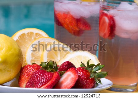 Two glasses of home made iced cold pink strawberry lemonade and plate full of fresh lemons, strawberries on hot summer on edge of swimming pool.