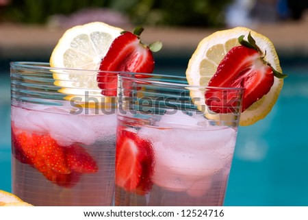 Two glasses of home made iced cold lemonade on hot summer on edge of swimming pool.