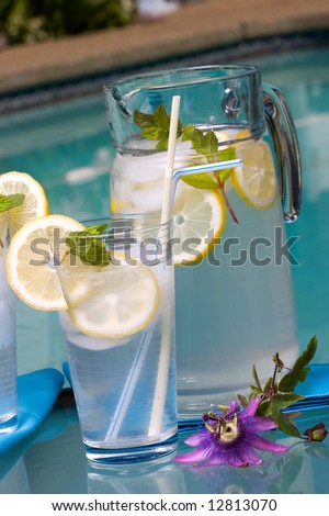 Two glasses of home made iced cold lemonade and pitcher on hot summer on edge of swimming pool.