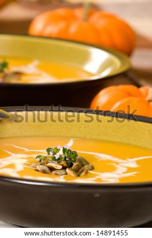 Closeup of bowl of hot delicious pumpkin soup garnished with cream, roasted pumpkin seeds and fresh thyme
