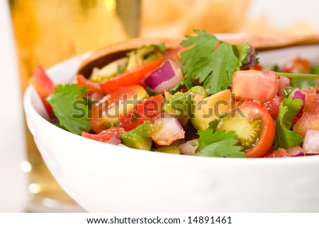 Closeup of a bowl with fresh cherry tomatoes and avocado salsa. Glass of beer out of focus.