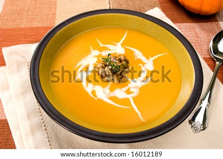 Bowl of hot delicious pumpkin soup garnished with cream, roasted pumpkin seeds and fresh thyme