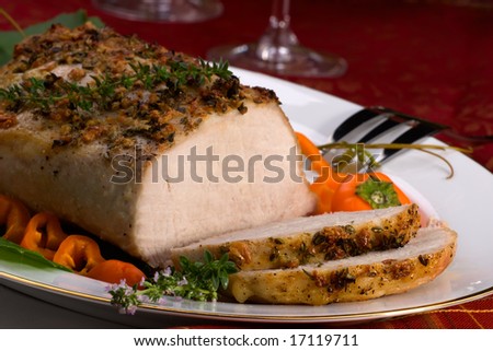 Delicious sliced garlic thyme roast pork loin and glass of red wine ready for Christmas dinner on holiday table.