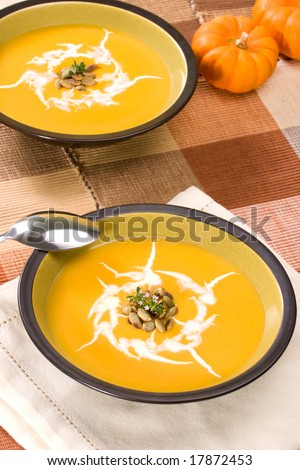 Closeup of bowl of hot delicious pumpkin soup garnished with cream, roasted pumpkin seeds and fresh thyme