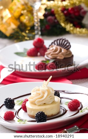 Delicious Vanilla Bean Cheesecake served with fresh raspberries, blackberries and mint. Chocolate cheesecake and Christmas ornament out of focus in background