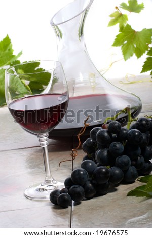 Glass of red wine, decanter and fresh cut black wine grape bunch.
