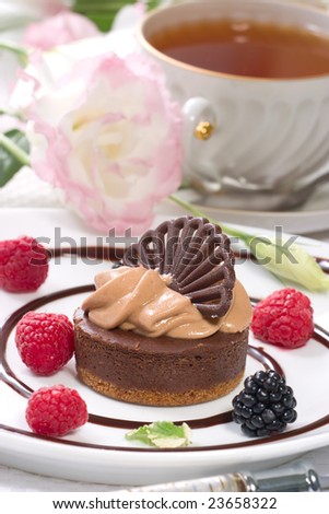 Delicious chocolate cheesecake served with fresh raspberries, blackberries and mint. Cup of tea and flowers.