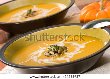 Two bowls of hot delicious pumpkin soup garnished with cream, roasted pumpkin seeds and fresh thyme