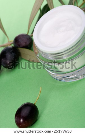 Closeup of jar of moisturizing face cream and twig with black olives.
