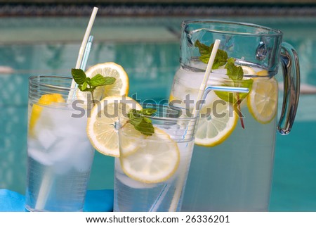 Two glasses of home made iced cold lemonade and pitcher on hot summer on edge of swimming pool.