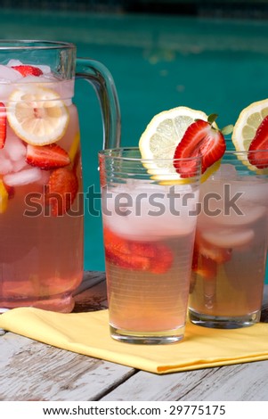 Two glasses of home made iced cold pink strawberry lemonade and pitcher on hot summer on edge of swimming pool.