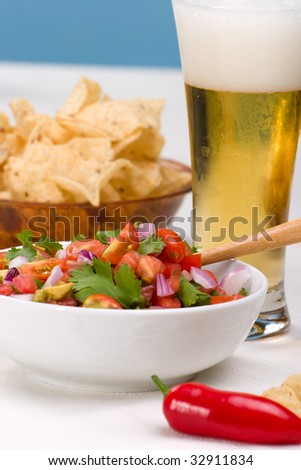 Bowl with fresh cherry tomatoes and avocado salsa. Corn chips and beer. Very shallow DOF on salsa.