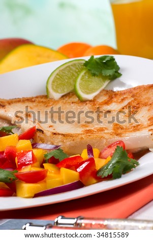 Closeup of fried skate (ray) with mango, cherry tomato and red onion salsa. Fresh fruits and glass of juice.