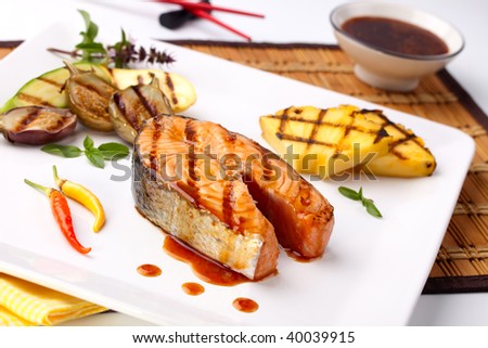 Delicious grilled Teriyaki salmon steak  garnished with grilled pineapple, baby eggplants, zucchini and chilli pepper for healthy style dinner.