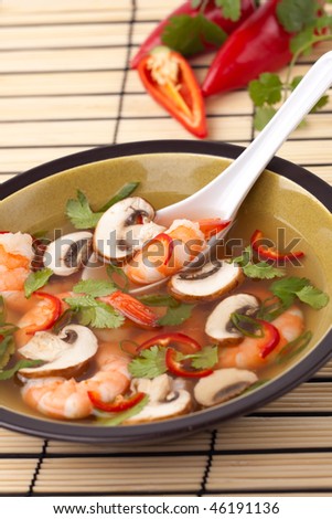 Closeup of a bowl of hot-and-sour prawn soup with mushrooms, prawns, chili pepper and cilantro.