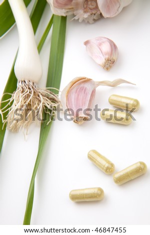 Closeup of garlic extract pills and fresh garlic leaves and cloves best suited for health, anti-cholesterol and alternative medicine ads