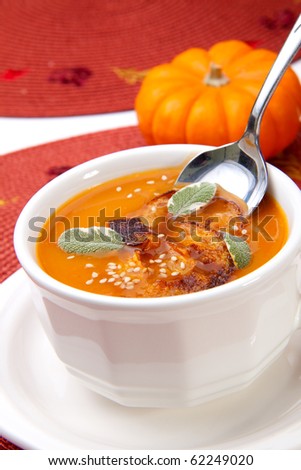Closeup of a cup of hot delicious spicy roasted pumpkin soup with pumpkin crisps, sage and sesame seeds.