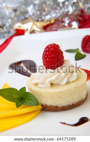 Delicious Vanilla Raspberry Cheesecake served with fresh mango and mint. Christmas ornament out of focus in background
