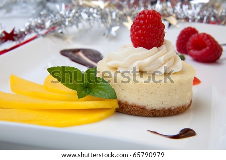 Delicious Vanilla Raspberry Cheesecake served with fresh mango and mint. Christmas ornament out of focus in background