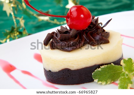 Closeup of delicious Chocolate Vanilla Cheesecake garnished with maraschino cherries and mint. Christmas ornament out of focus in background