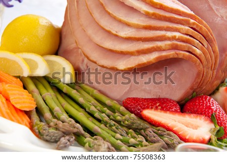 Close up of glazed ham for Easter celebration dinner garnished with asparagus, strawberry, and lemon wedges.