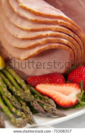 Close up of glazed ham for Easter celebration dinner garnished with asparagus, strawberry, and lemon wedges.