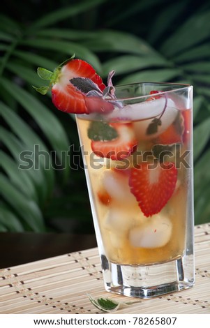 Closeup of glass of strawberry and sage iced tea on a table in a restaurant on a tropical beach.