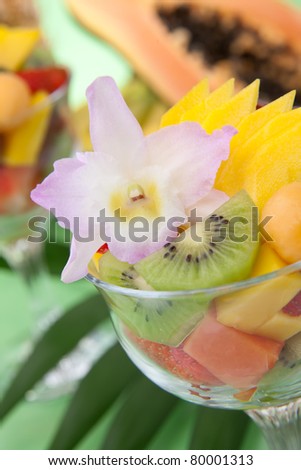 Closeup of serving of fresh tropical fruit salad in cocktail glass. Kiwi, melon, papaya, mango, red grapes, strawberry and orchid flower.