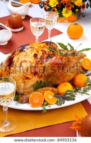 Garnished citrus glazed roasted turkey on holiday table, pumpkins, flowers, and white wine