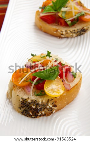Closeup of two delicious yellow, red, and orange tomato Bruschetta garnished with Parmesan cheese and fresh basil leaves.